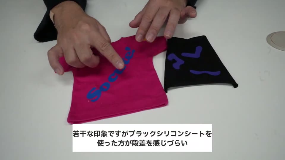 ピンクのTシャツと黒いTシャツにラバーシートで青い文字を貼り、触って比べているところ