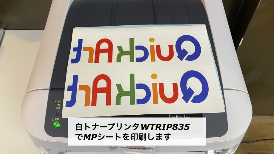 白トナープリンタWTRIP835から、左右反転したカラーのQuickArtのロゴを印刷したMPシートが出てくる様子