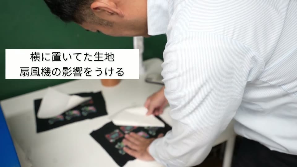 横に置いていたTシャツから転写紙を剥がしている。テロップに「横に置いてた生地 扇風機の影響をうける」