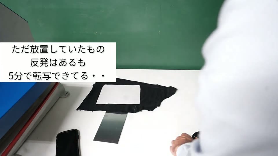 何もしないで5分置いた黒いTシャツから転写紙を剥がしているところ。テロップに「ただ放置していたもの 反発はあるも5分で転写できてる」