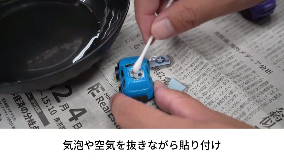青いミニカーに貼ったサッカーボールのデカールを、濡らした綿棒で押さえている手元