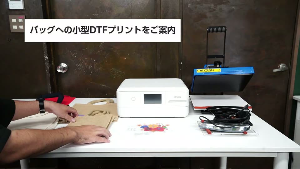 小型DTFプリンターWIP754、ミニプレス機、家庭用アイロン、無地のバッグを机に並べた様子