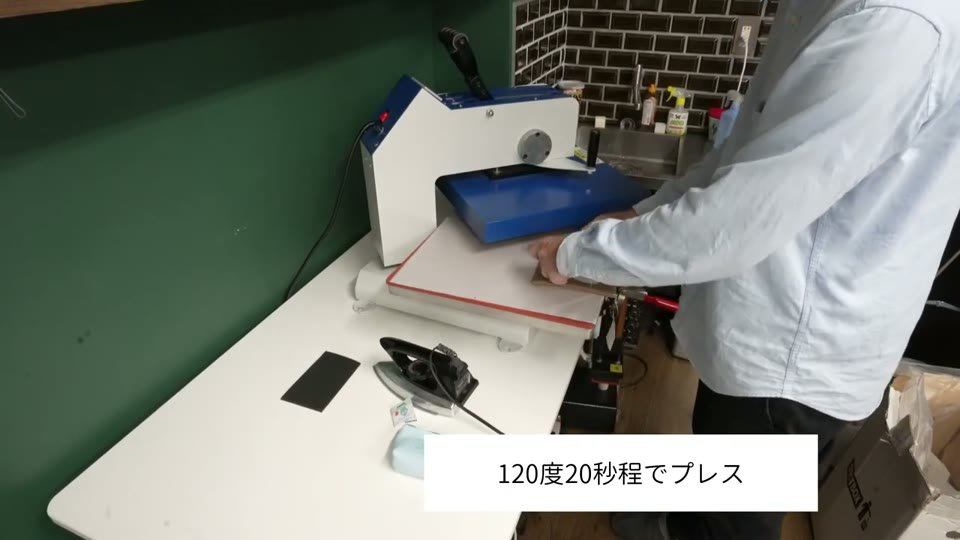 スウィング式の熱プレス機でベージュのポーチをプレスしている様子。テロップに「120度20秒程でプレス」