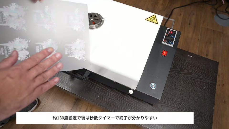 引き出し式のベイキングマシンにパウダーを付けたDTFフィルムを入れようとしている様子。温度表示のパネルが見える