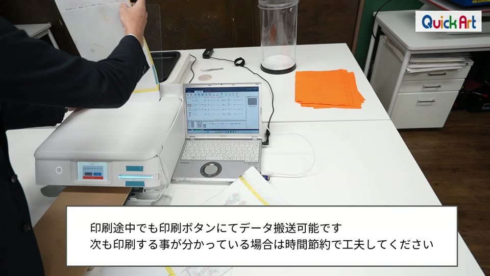 小型DTFプリンターにキャリーシートをセットする様子。印刷途中でも印刷ボタンにてデータ搬送可能です、次も印刷する事が分かっている場合は時間節約で工夫してくださいというテロップ