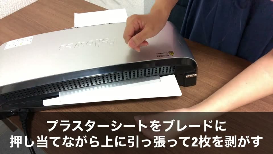 抜けるラミネーターの出口で、プラスターシートを手前のブレードに押し当てながら引き上げている。テロップはプラスターシートをブレードに押し当てながら上に引っ張って2枚を剥がす
