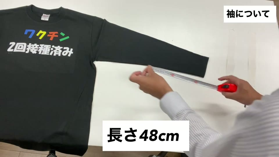 Mサイズの黒いロンTの袖の長さをメジャーで測っている様子。長さ48cmとテロップが出ている