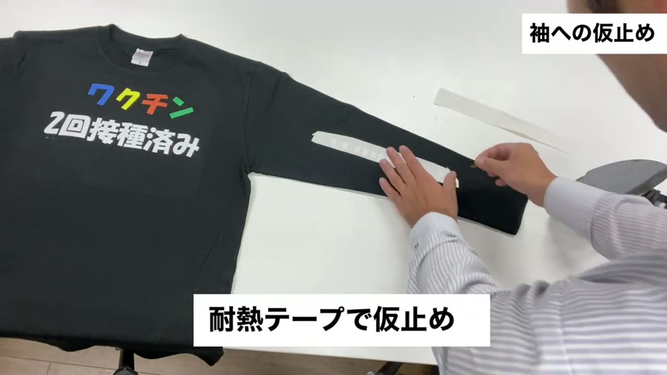 ロンTの袖に置いた細長い転写マークを耐熱テープで留めている様子。耐熱テープで仮止めとテロップが出ている