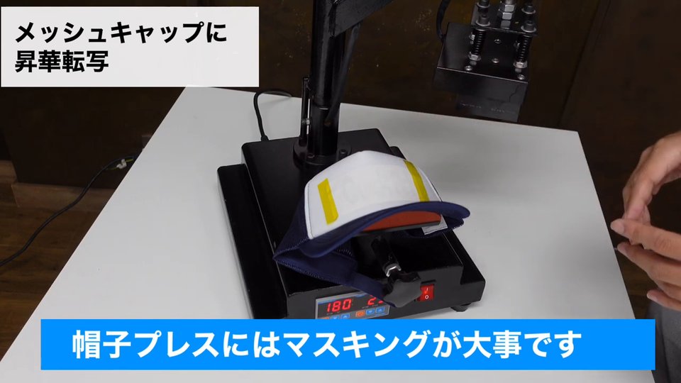 メッシュキャップに転写紙を当て、左右を黄色い耐熱テープで留めている。テロップ:帽子プレスにはマスキングが大事です