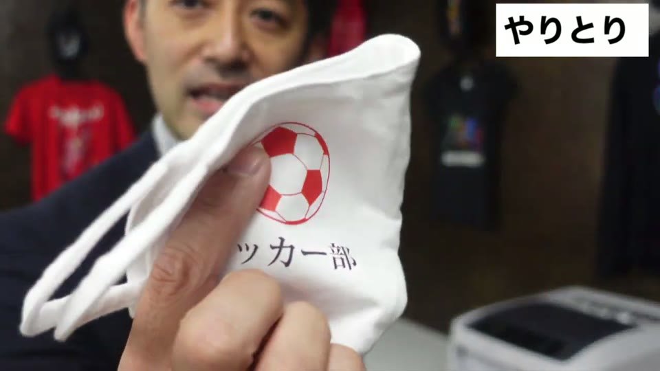 赤いサッカーボールの絵がプリントされた白い布をカメラに近づけて見せている場面