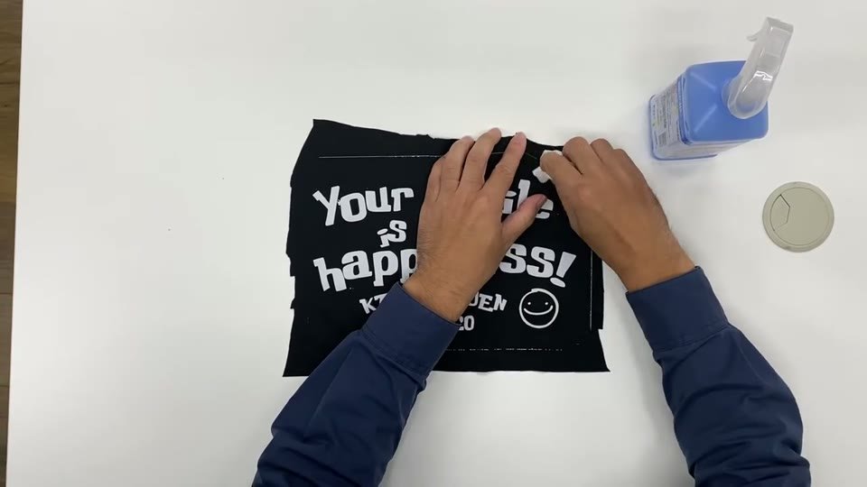 エタノールのスプレーボトルを横に置き、黒い布にプリントした白い文字のまわりを指先でこすっている手元