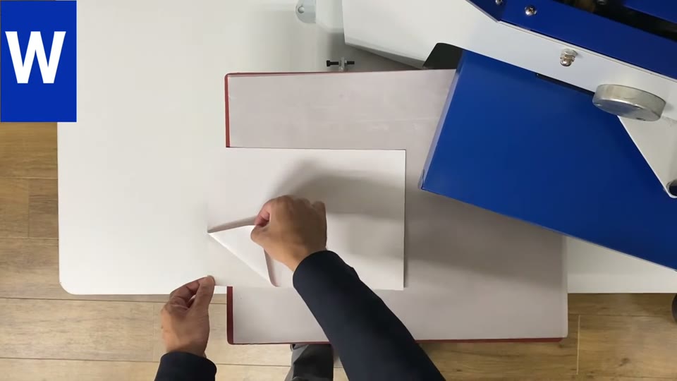 プレス機の上でタイプWのシートの角をつまんで剥がし始めているところを真上から撮影