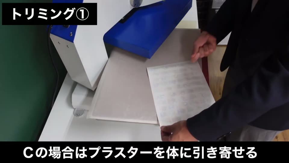 プレス台の上でプラスターシートを体のほうへ引き寄せるように剥がしている手元。テロップはCの場合はプラスターを体に引き寄せる