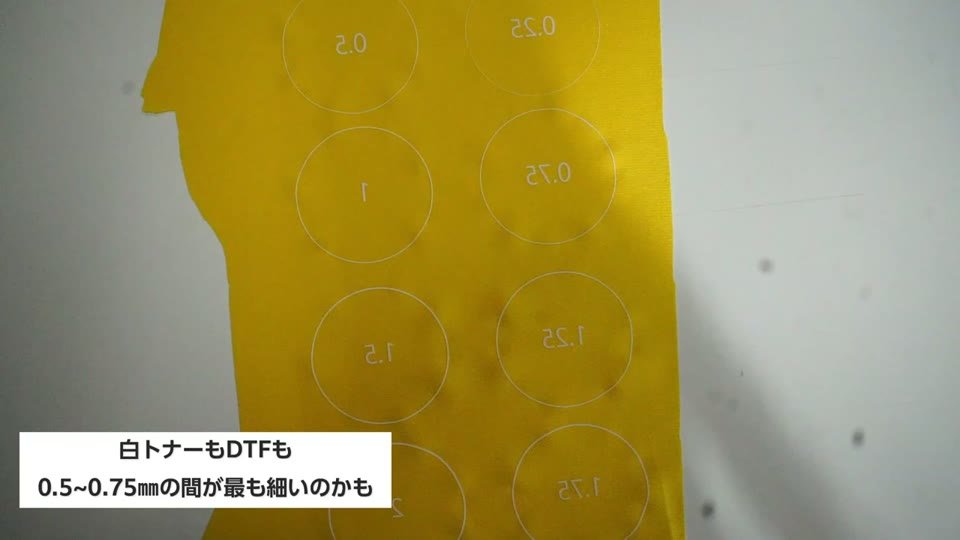 黄色の生地に白トナーでプリントした円の線と、白トナーもDTFも0.5から0.75mmの間が最も細いのかもというテロップ