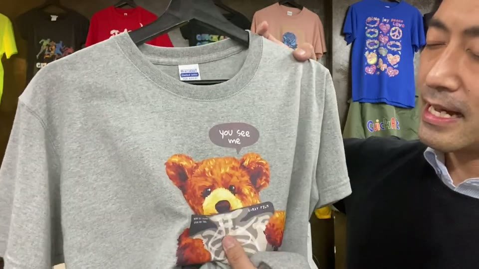 グレーのTシャツにプリントしたクマのイラストを、指で触って見せている場面