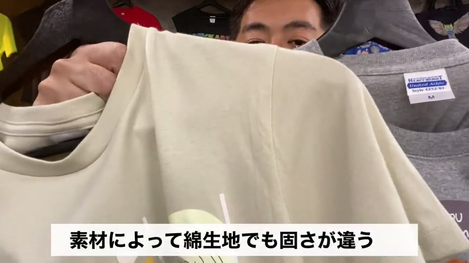 生成りのTシャツの肩を持ち上げ、「素材によって綿生地でも固さが違う」とテロップが出ている場面