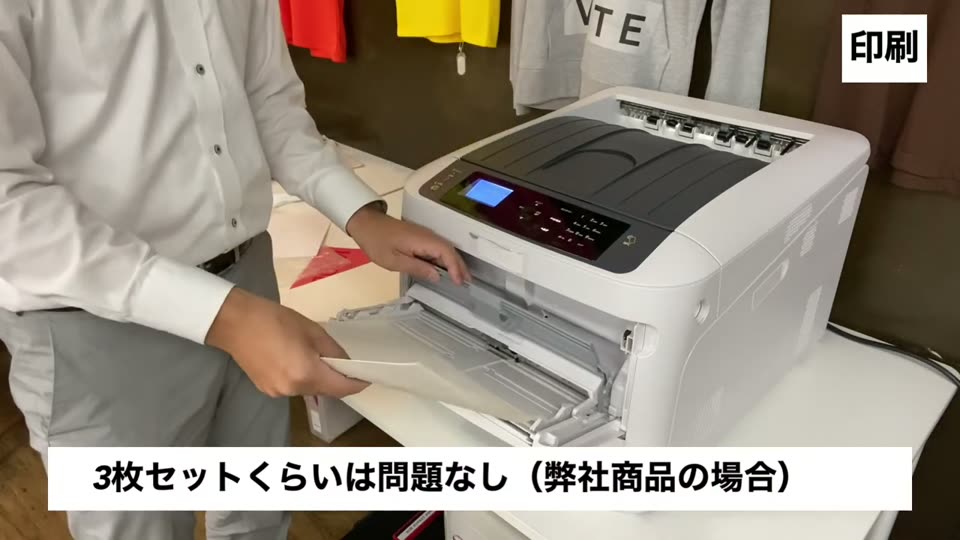 白トナープリンタの手差しトレイに転写紙をセットする様子。3枚セットくらいは問題なし(弊社商品の場合)というテロップ