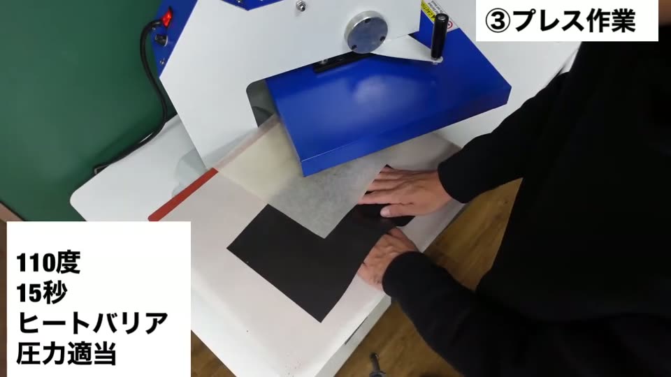プレス機の下台に木材とマークを置き、上に黒いヒートバリアマットを敷いている。110度・15秒・ヒートバリア・圧力適当のテロップ